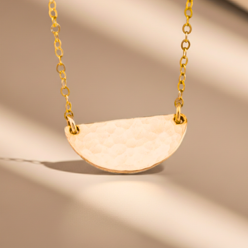 Gold necklace with a half-circle pendant on a beige background