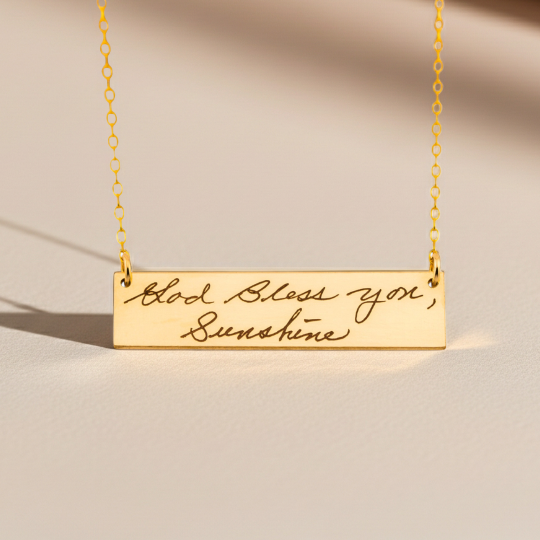 Gold necklace with engraved message on a beige background