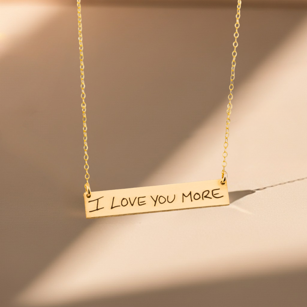 Gold necklace with 'I LOVE YOU MORE' pendant on a beige background