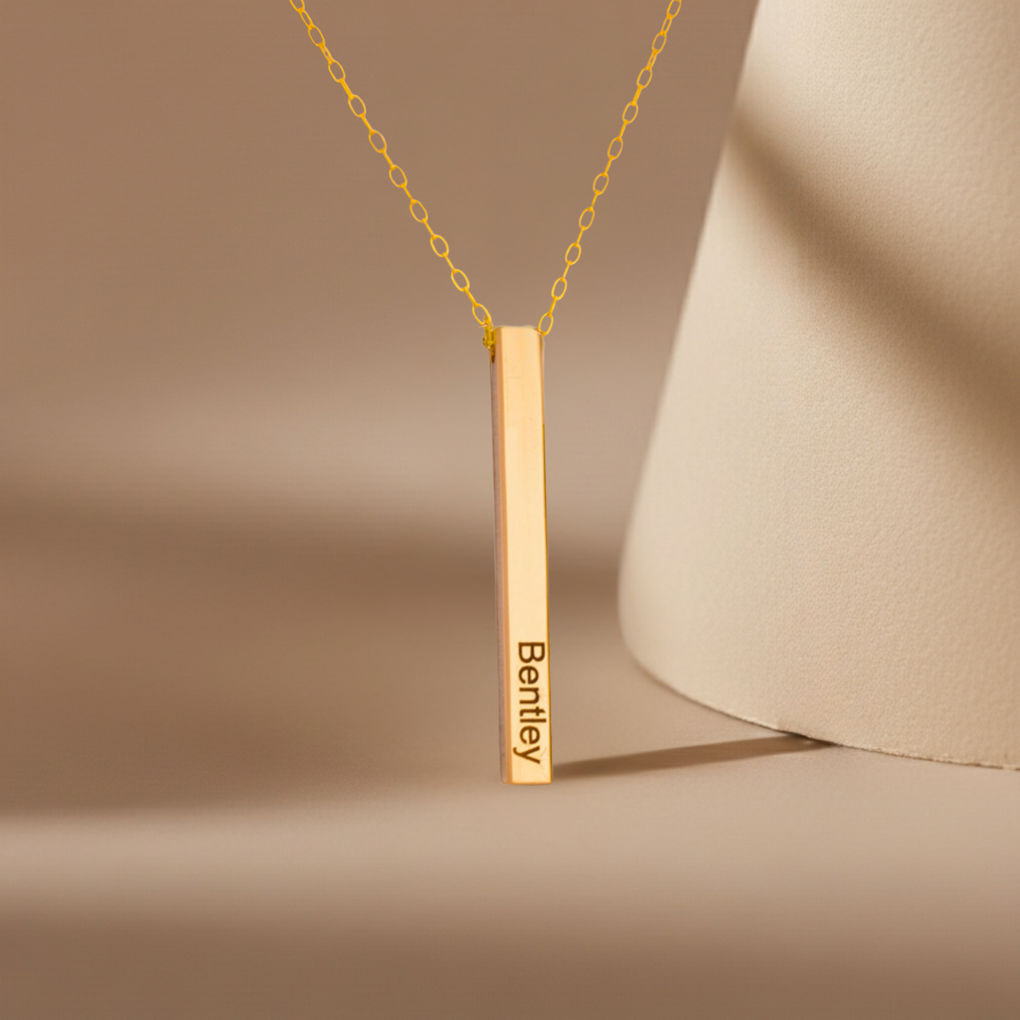 Gold necklace with a vertical bar pendant on a beige background